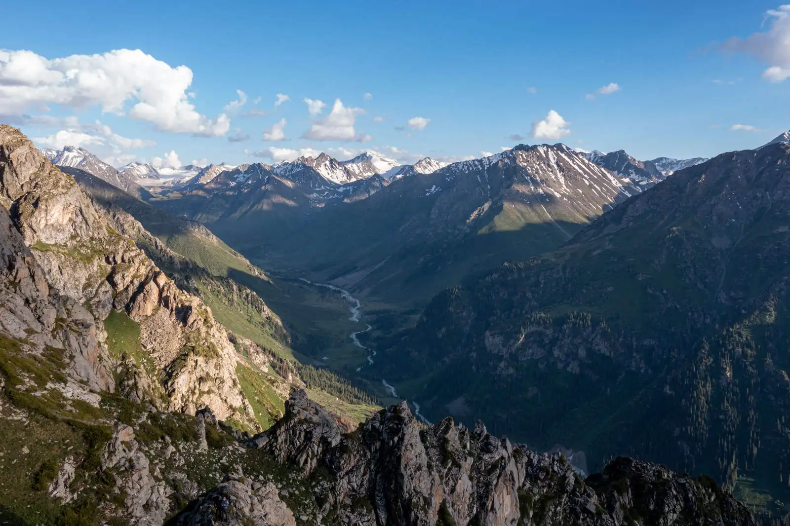 Panoramic mountain valley view with a winding river and snow-patched peaks near Almaty